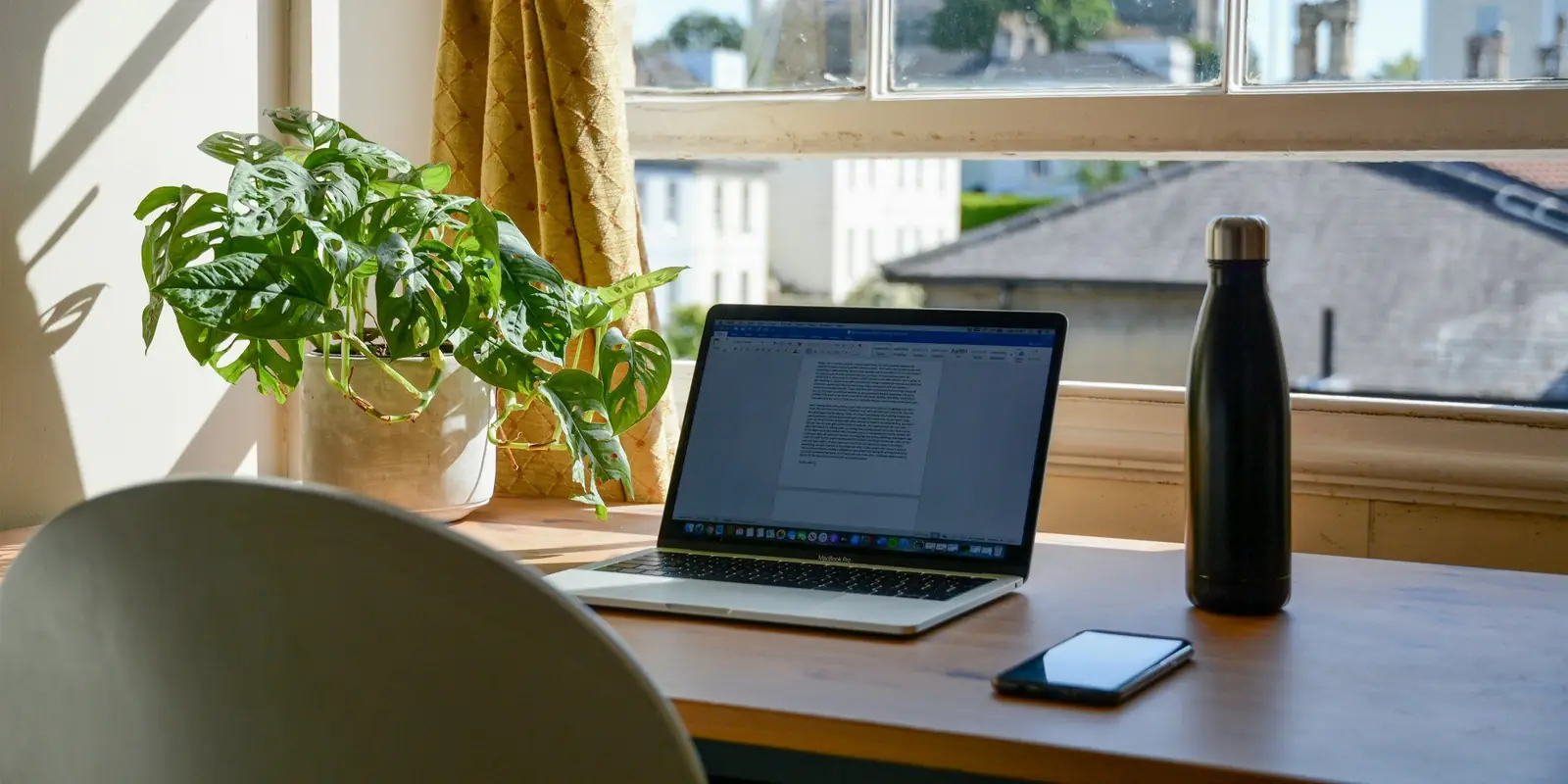 A laptop and phone on a desk by a sunny window